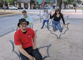 four students sitting on metal bat sculptures in city setting