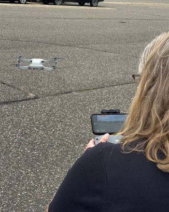 woman with controls for a drone with the drone in the air in front of her