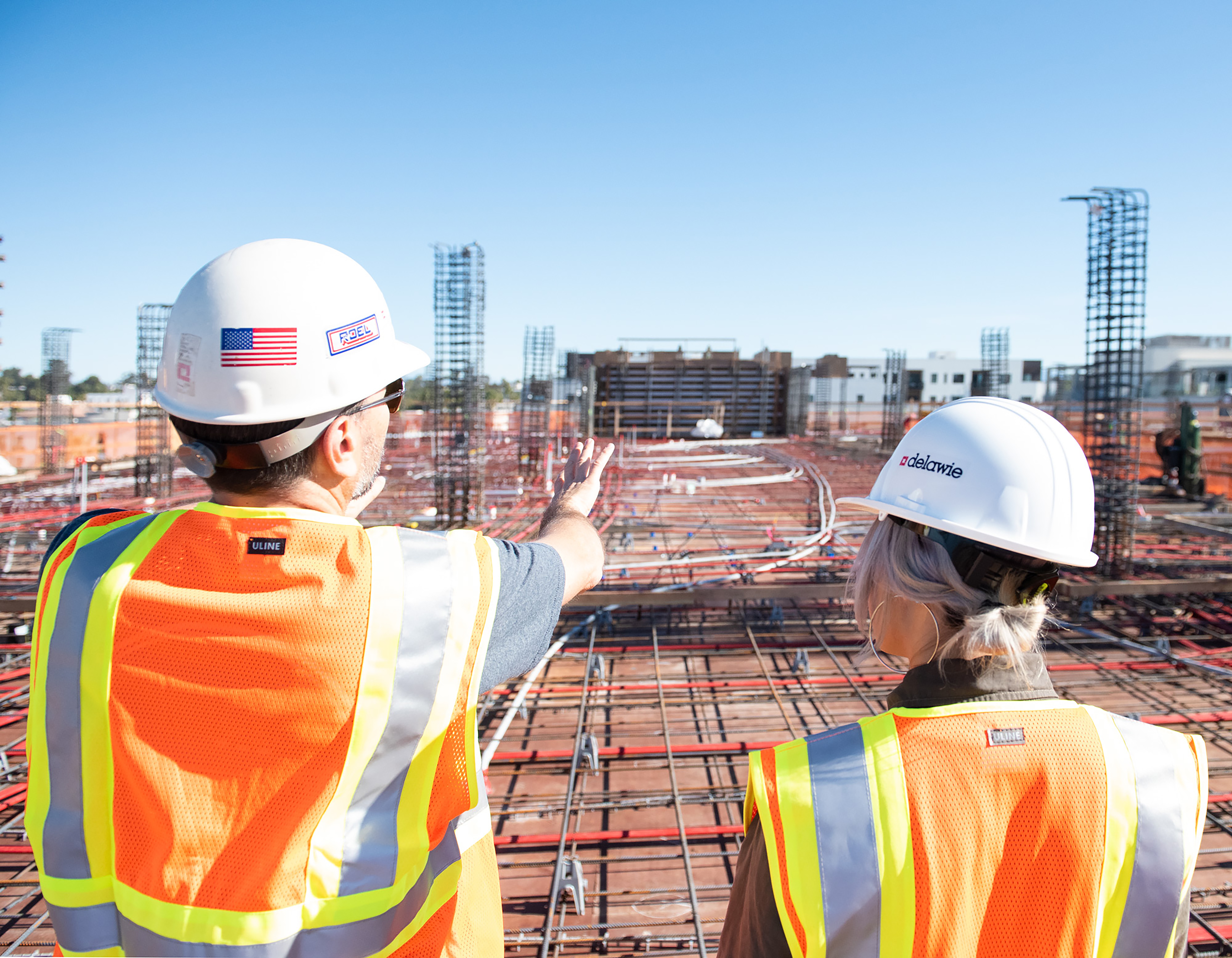 two people talking and standing outside at a construction job site wearing safety vests and hard hats